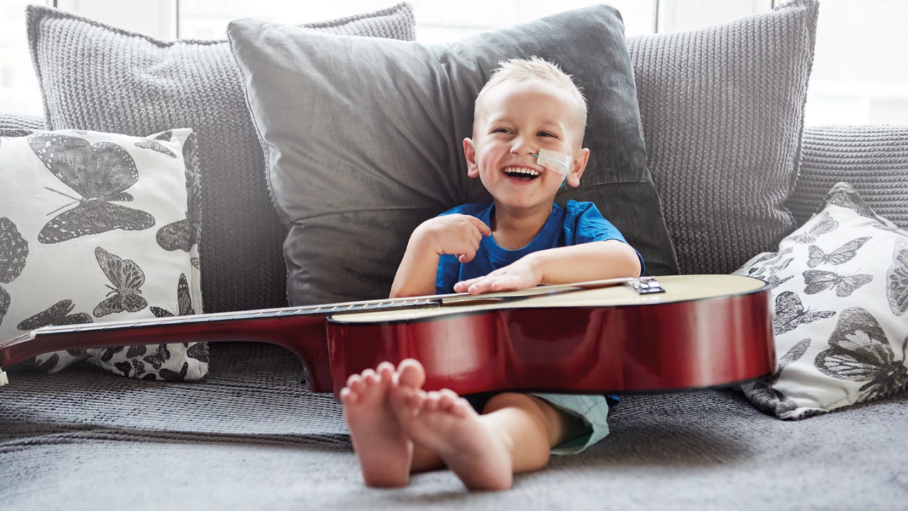 Smiling toddler sitting on a couch, holding a guitar